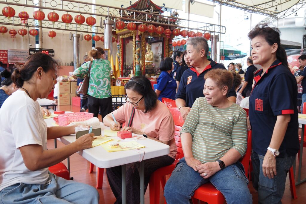 ผู้ร่วมงานกรอกข้อมูลทำบุญโดยมีอาสาสมัครอำนวยความสะดวก ปี 2568