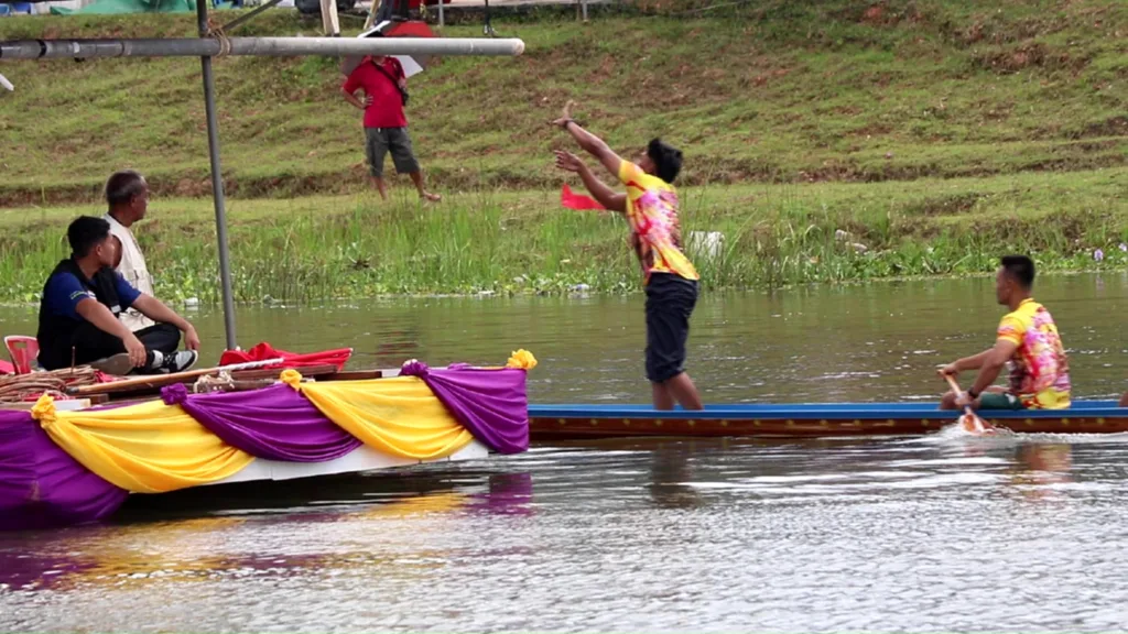 ผู้แข่งขันยืนขึ้นจากโขนหัวเรือเพื่อเอื้อมชิงธงที่จุดตัดสินในงานปี 2568