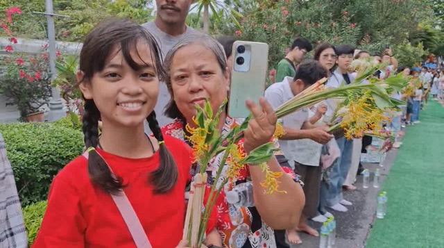 ผู้ร่วมงานถือดอกเข้าพรรษารอถวายพระสงฆ์บริเวณวัดพระพุทธบาทในปี 2568