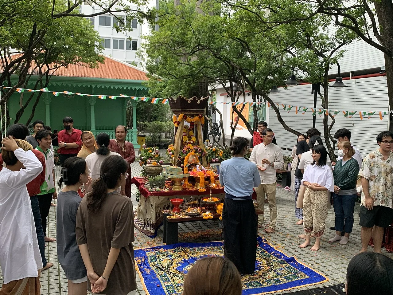 ผู้ร่วมงานยืนรอบโต๊ะบูชาพระคเณศที่ประดับดอกไม้ในลานมหาวิทยาลัยศิลปากร กรุงเทพฯ