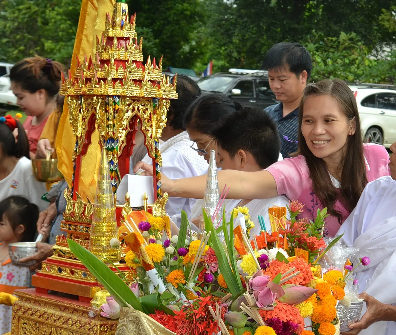 ผู้ร่วมงานตักบาตรเทโวถือภาชนะและถวายสิ่งของบริเวณขบวนที่ประดับดอกไม้