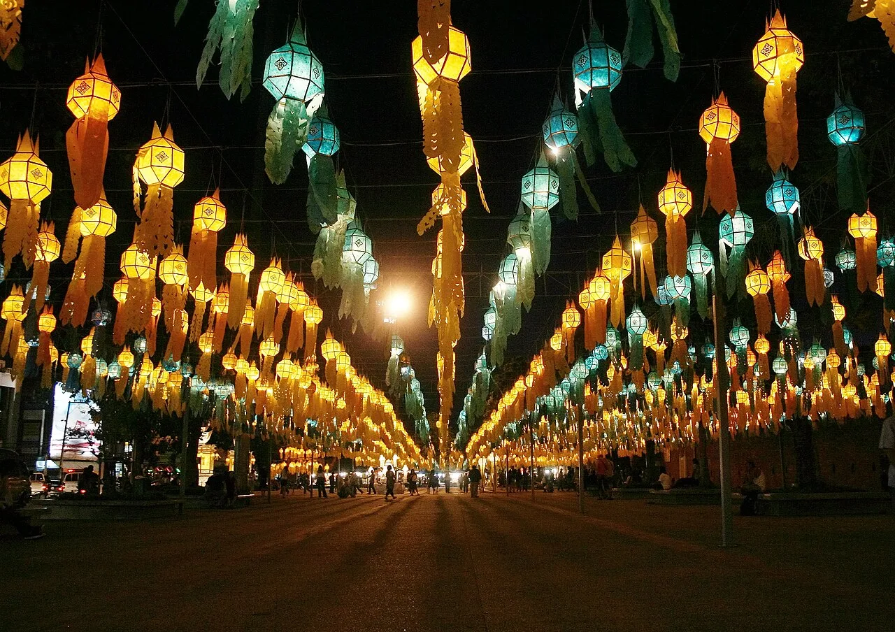 โคมกระดาษสีเหลืองและสีเขียวอมฟ้าแขวนเรียงหลายแถวเหนือพื้นที่เดิน มีหางกระดาษห้อยลงมาและแสงไฟในยามค่ำ