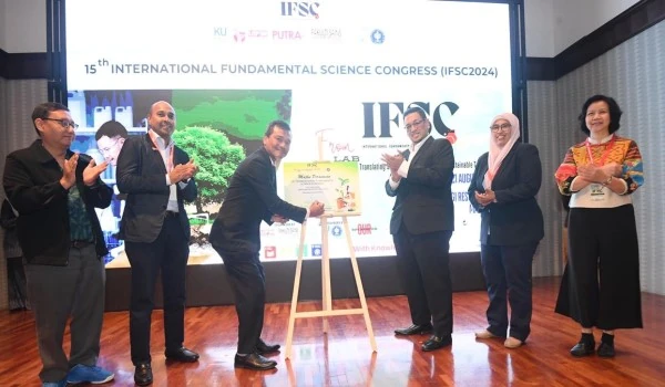 ผู้ร่วมงานยืนบนเวทีในพิธีเปิด IFSC2024 โดยมีป้าย 15th International Fundamental Science Congress ด้านหลัง