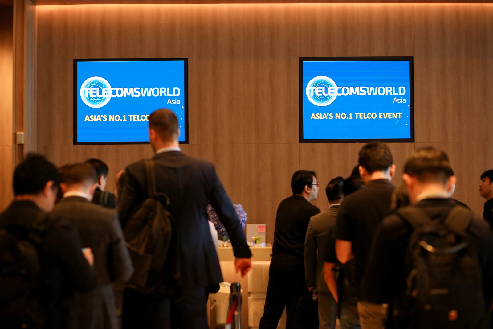 ผู้เข้าร่วมเดินเข้าสู่งาน Telecoms World Asia 2025 ที่มีป้ายงานปี 2025