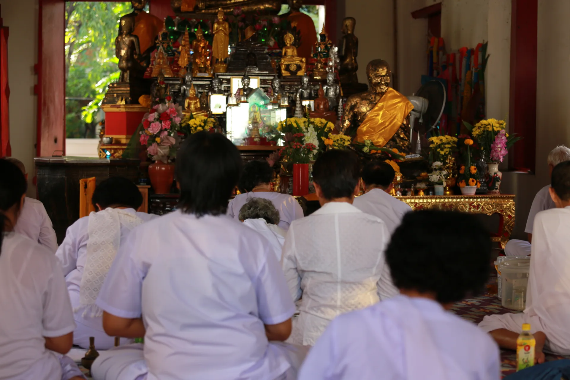 ผู้ร่วมกิจกรรมนั่งหันหน้าไปทางพระประธานภายในอุโบสถระหว่างสวดมนต์