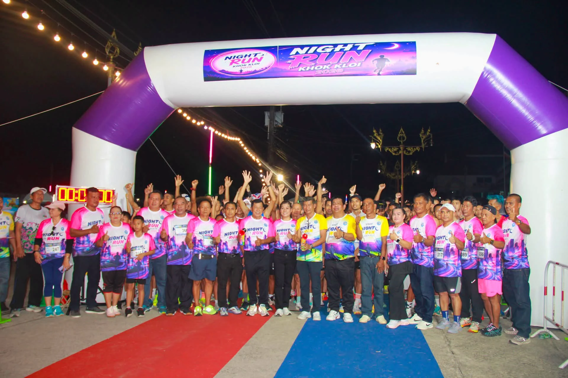 ผู้ร่วมงานสวมเสื้อไนท์รันโคกกลอยยืนบริเวณซุ้ม NIGHT RUN KHOK KLOI 2026 ในเวลากลางคืน