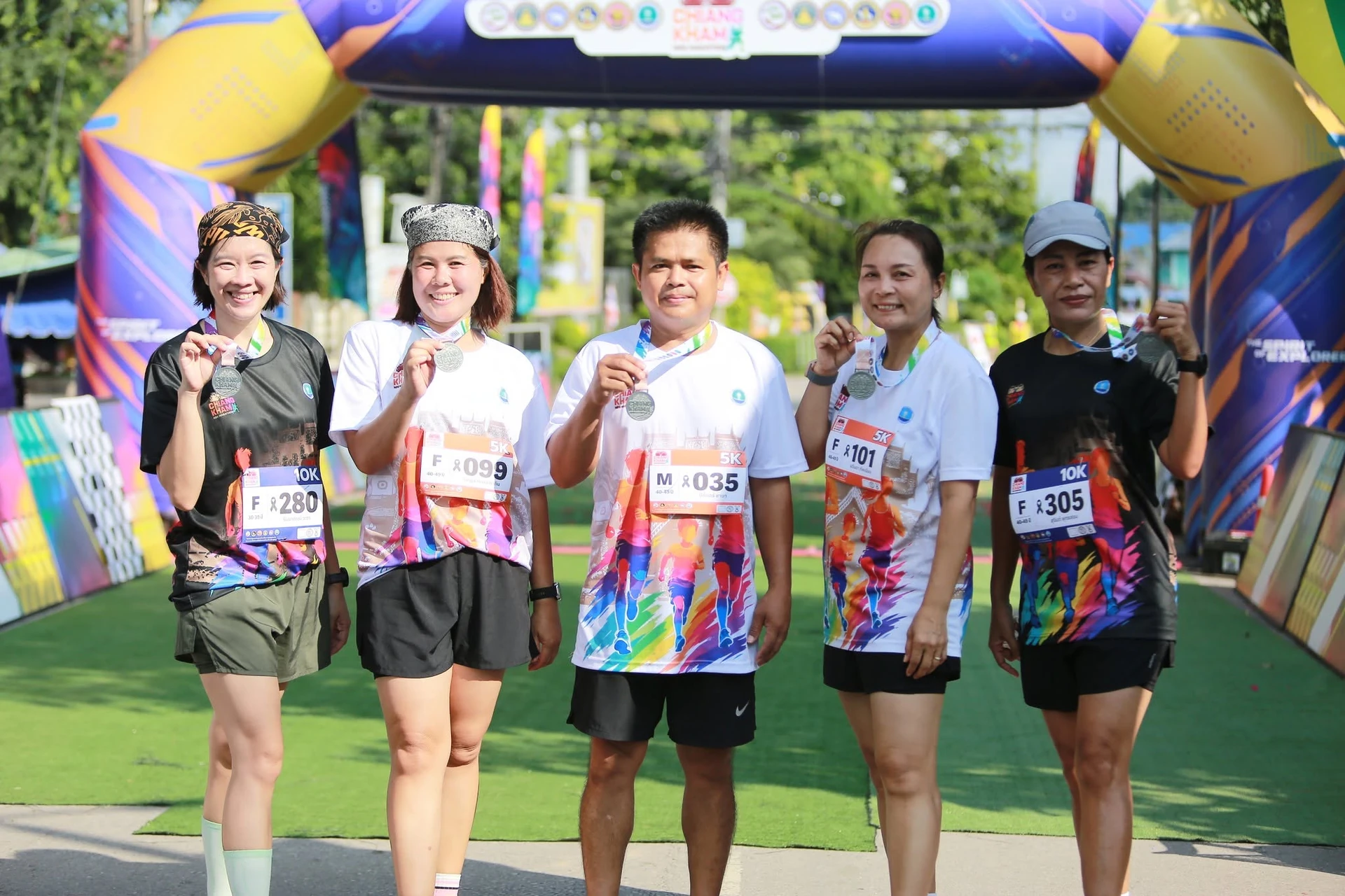 ผู้ร่วมงานกลุ่มหนึ่งถือเหรียญบริเวณซุ้ม ChiangKham Mini Marathon ในอัลบั้มกิจกรรมปี 2569