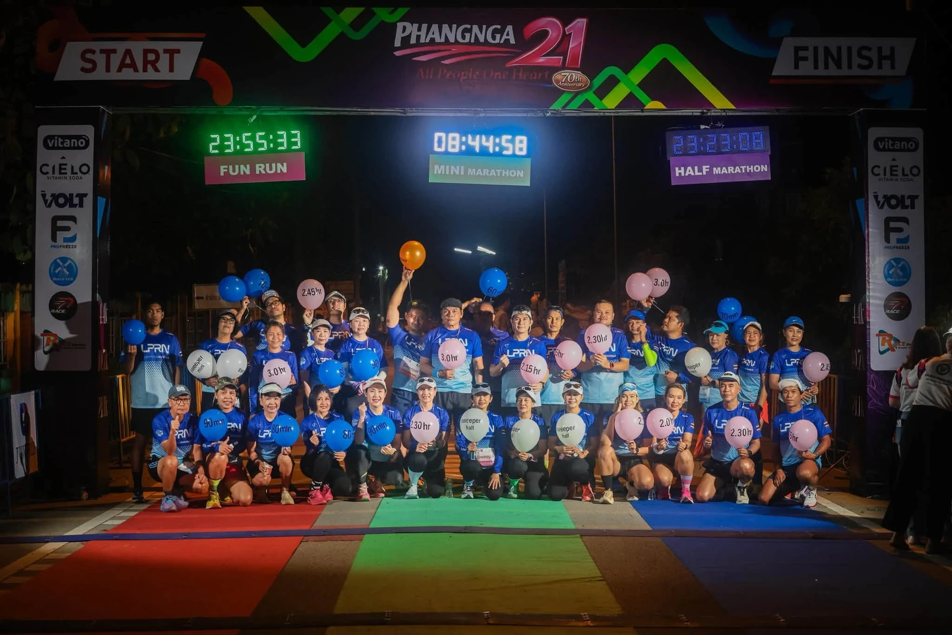 ผู้ร่วมกิจกรรมยืนบริเวณซุ้ม START FINISH ที่มีชื่อ PHANGNGA21 พร้อมลูกโป่งสีฟ้า จากโพสต์เพจผู้จัด
