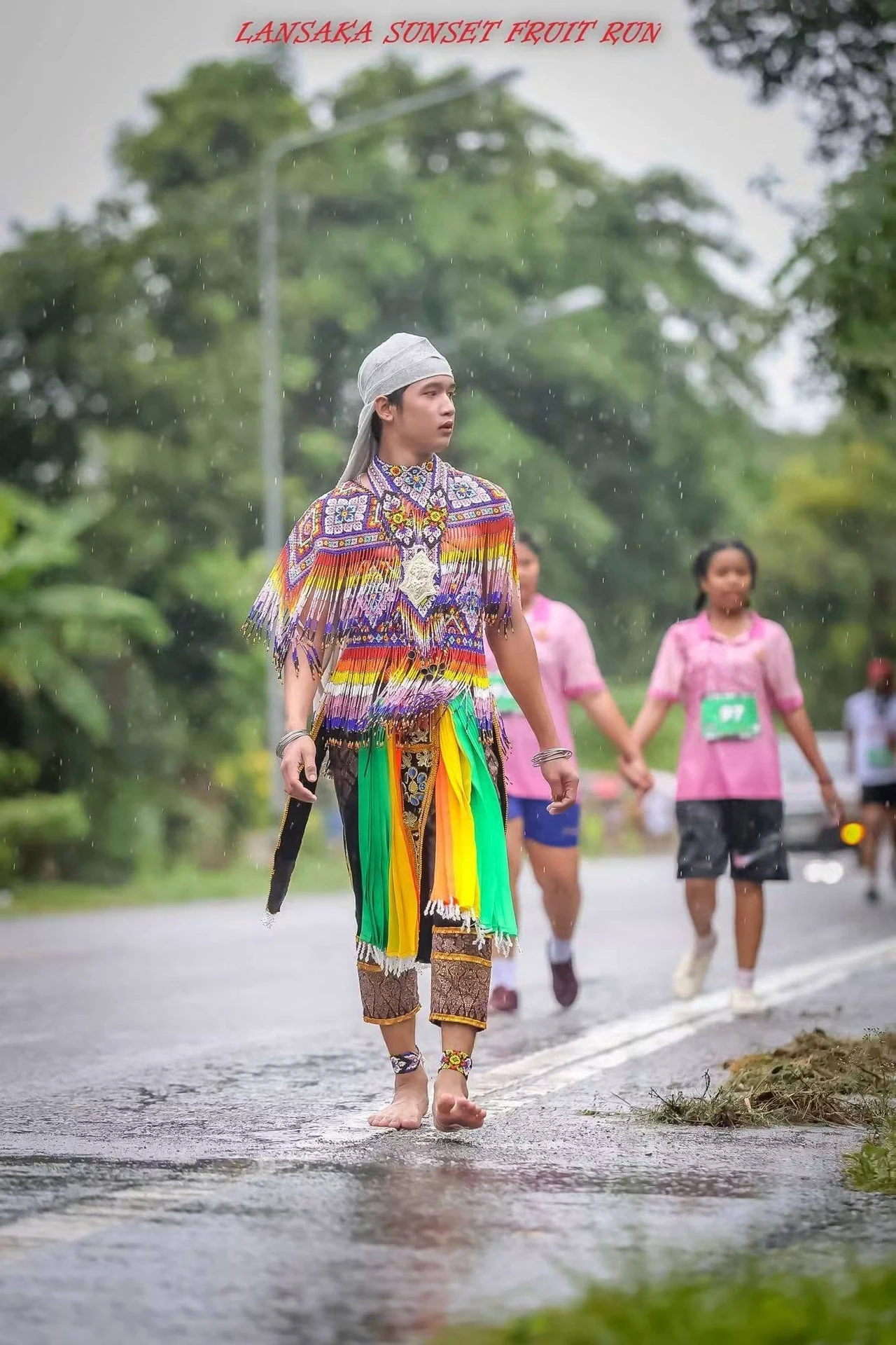 ผู้ร่วมกิจกรรมบนถนนเปียกในภาพแนวตั้งเต็ม จากโพสต์หลังงาน Lansaka Sunset Fruit Run ปี 2569