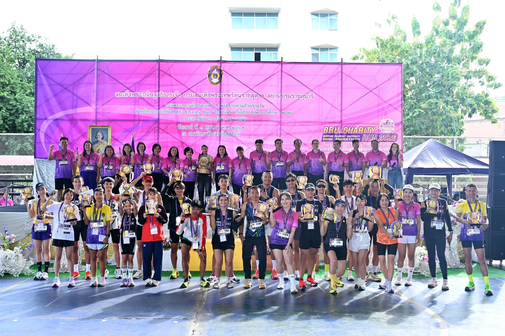 ผู้ร่วมกิจกรรมถ่ายภาพหน้าเวที BRU Charity Run ปี 2569 พร้อมถ้วยรางวัล