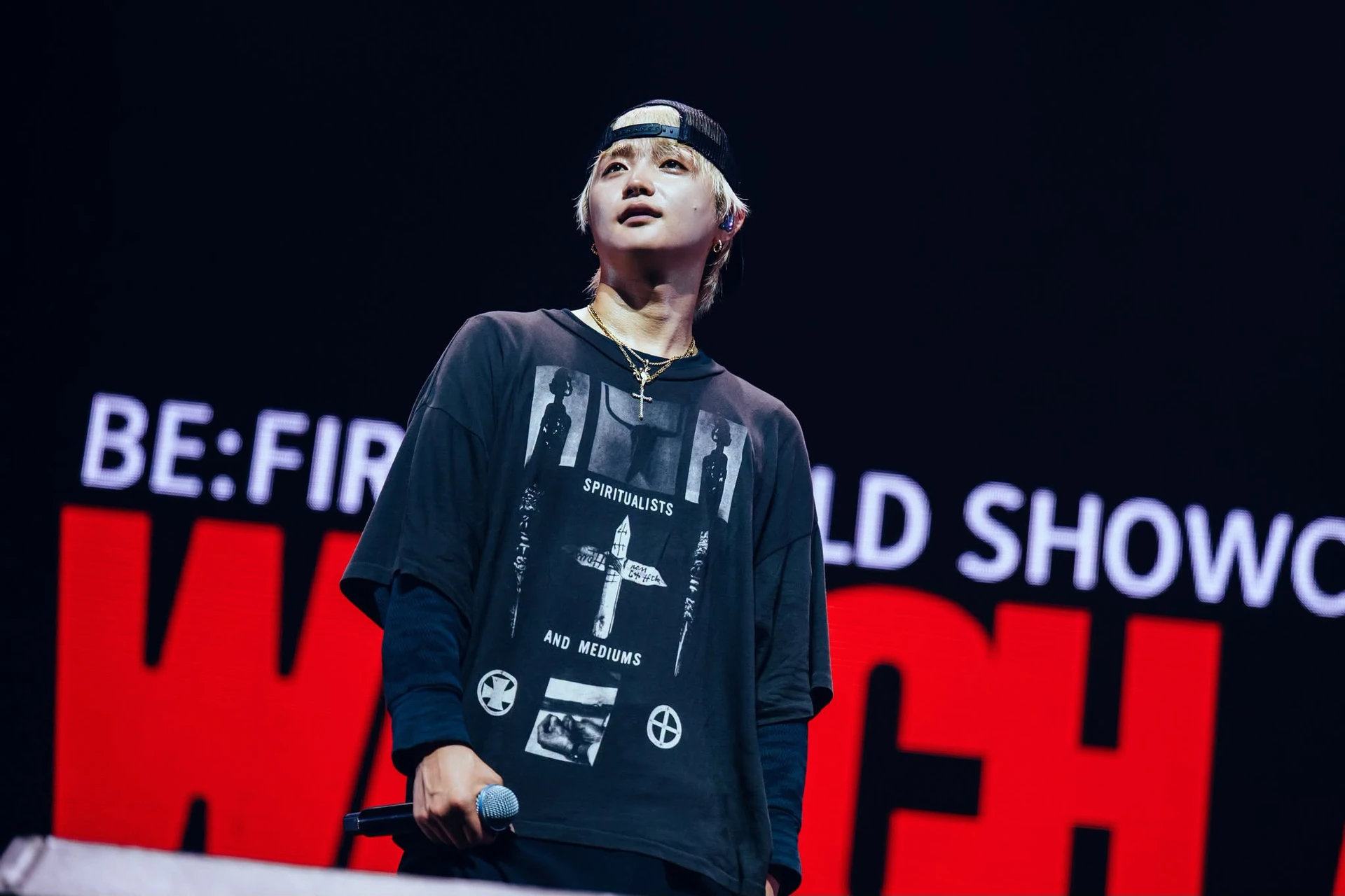 ศิลปินถือไมโครโฟนบนเวทีที่มีข้อความ BE:FIRST WORLD SHOWCASE WATCH ME จากชุดรายงานกรุงเทพฯ ปี 2569