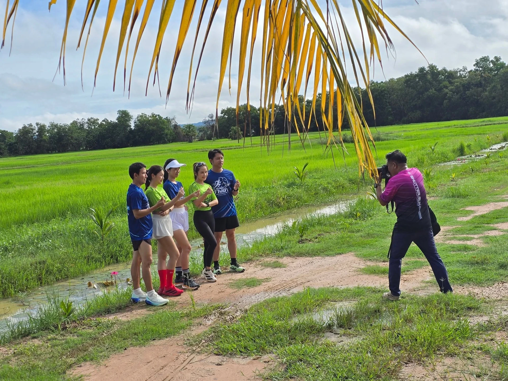 เบื้องหลังช่างภาพกำลังถ่ายภาพกลุ่มผู้ร่วมประชาสัมพันธ์งานทุ่งพระยามินิมาราธอนบริเวณทุ่งนา
