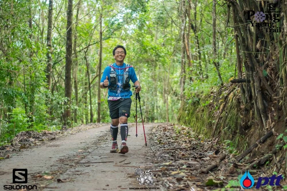 นักวิ่งถือไม้เทรลบนทางผ่านป่าในชุดภาพกิจกรรมครั้งก่อนของ Pong Yaeng Trail