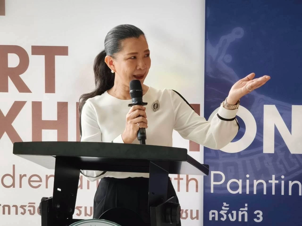 ช่วงใช้ไมโครโฟนที่แท่นในชุดภาพเปิดนิทรรศการจิตรกรรมเด็กและเยาวชน ครั้งที่ 3 ปี 2569