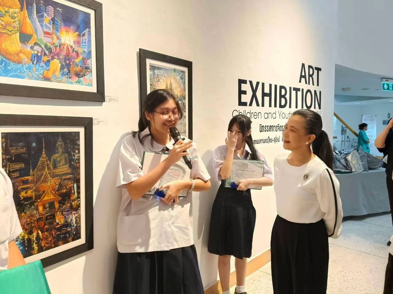 ผู้ร่วมกิจกรรมใช้ไมโครโฟนบริเวณผลงานและป้ายนิทรรศการจิตรกรรมเด็กและเยาวชน ครั้งที่ 3