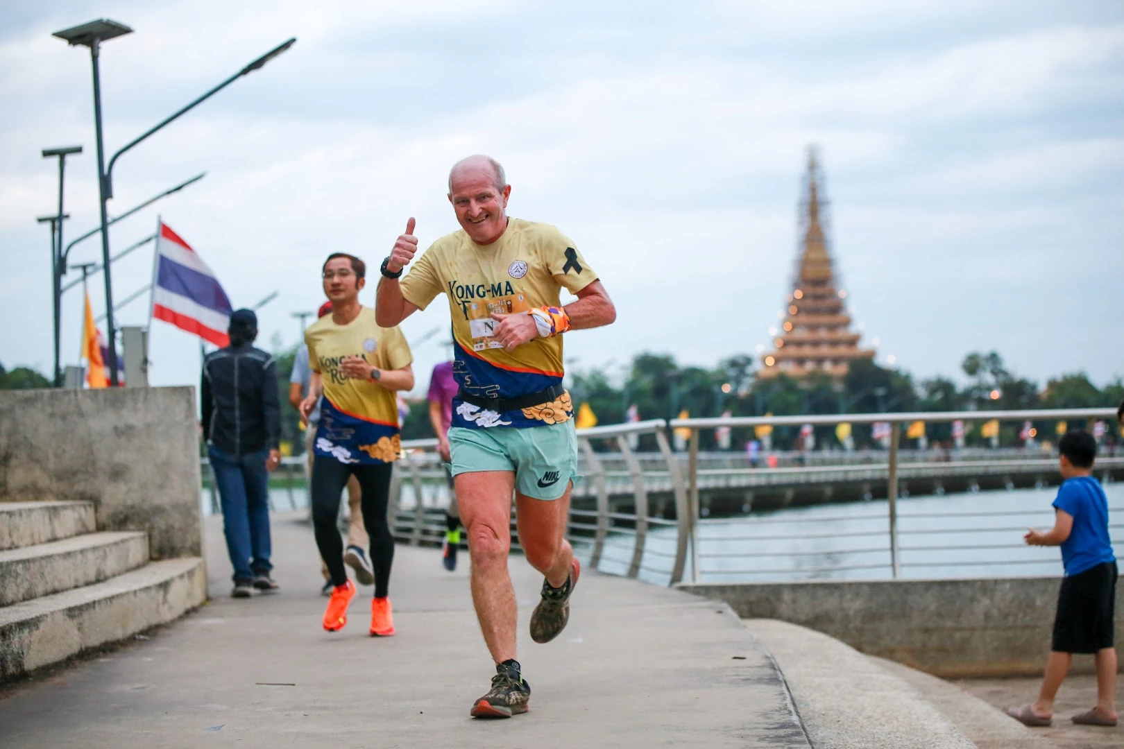 นักวิ่งสวมเสื้อ KONG-MA RUN หลายคนบนทางริมบึงในภาพที่แปดของอัลบั้มปี 2568