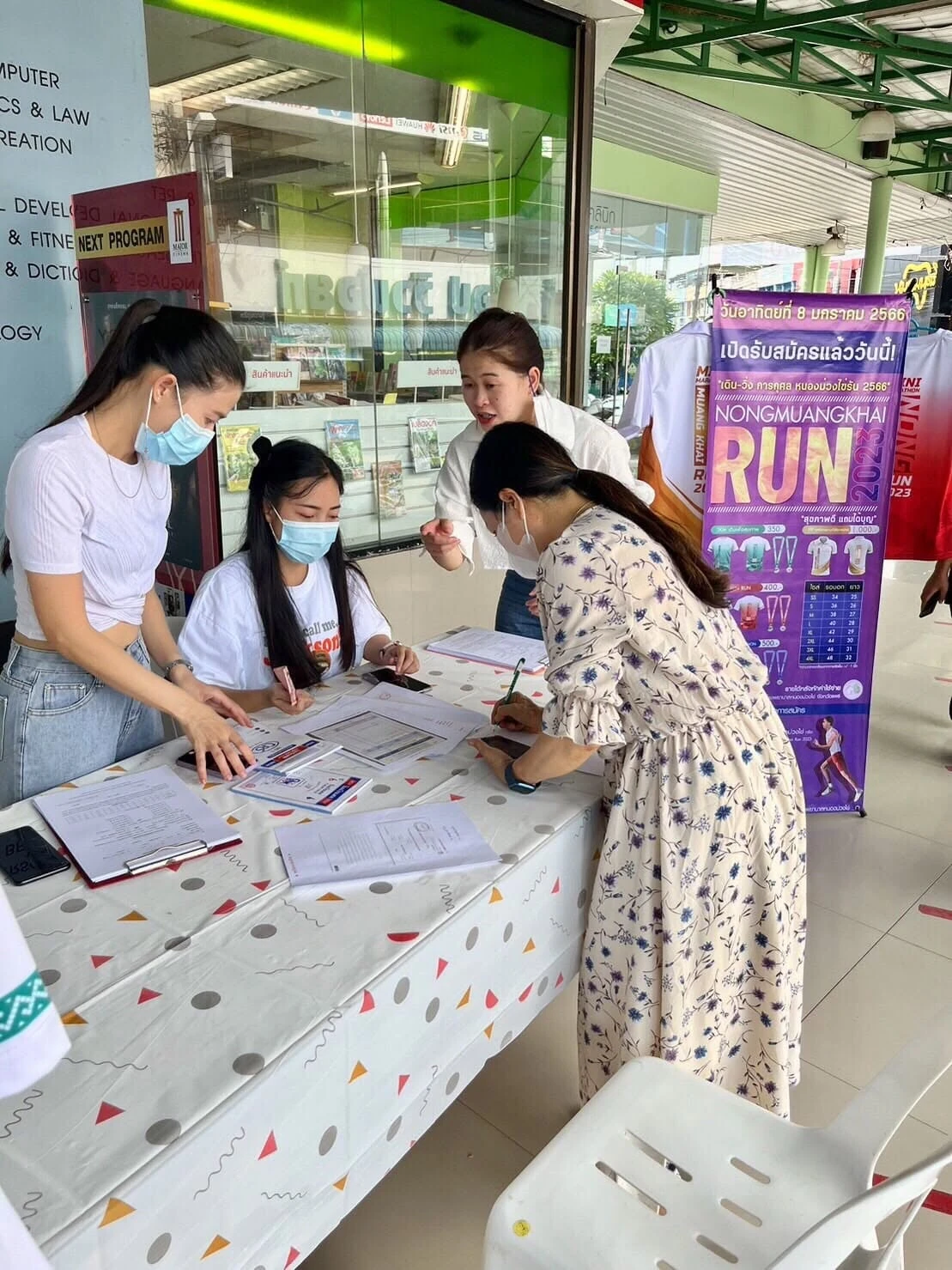 ภาพอีกมุมของจุดรับสมัครนอกสถานที่ พร้อมป้ายโครงการหนองม่วงไข่รันปี 2566 จากรายงานเดียวกัน คงภาพเต็ม