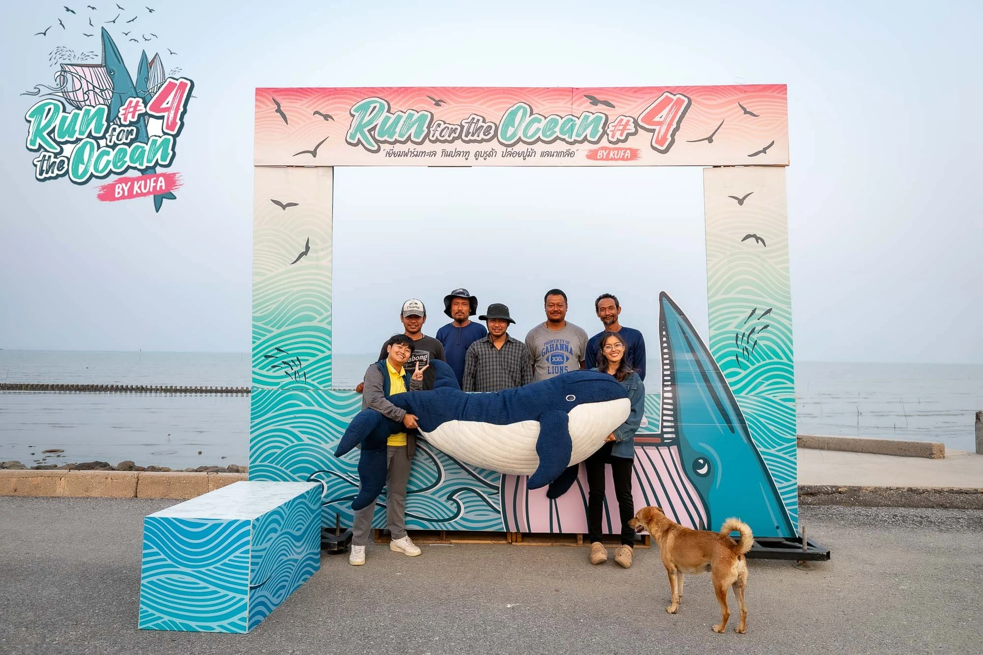 กลุ่มคนกับตุ๊กตาวาฬและฉาก Run for the Ocean ครั้งที่ 4 บริเวณริมน้ำ จากอัลบั้มรับเสื้อและ BIB คงภาพเต็ม ไม่ใช่งานครั้งที่ 5