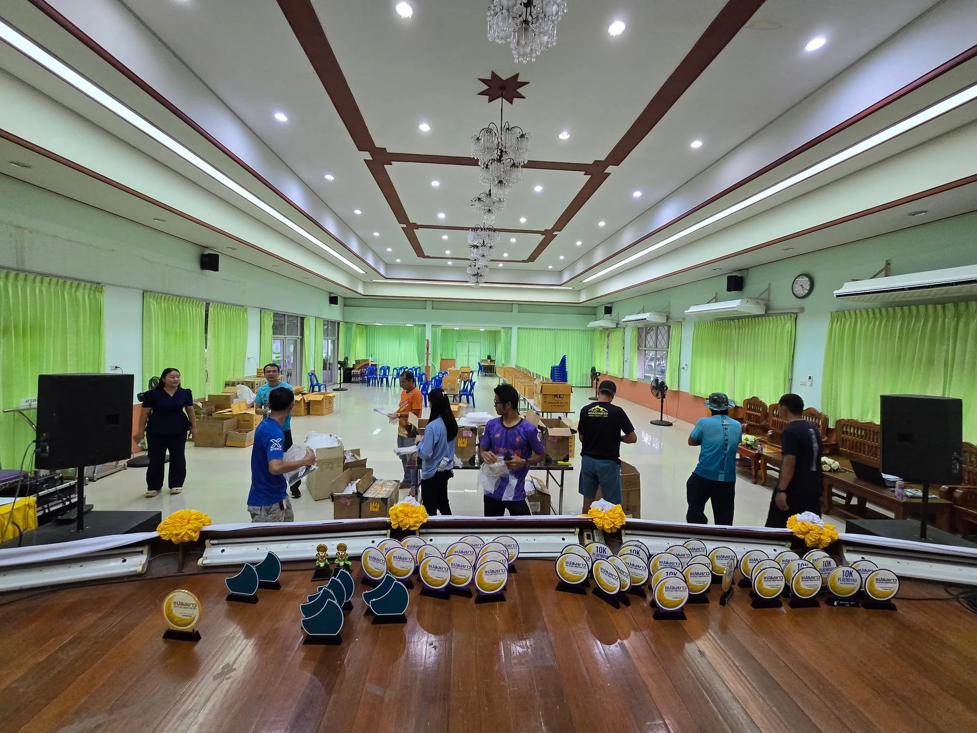 บรรยากาศจัดเตรียมของในหอประชุม พร้อมถ้วยรางวัลด้านหน้า จากชุดภาพเตรียมงานแปลงยาวครั้งก่อน ไม่ใช่ภาพวันแข่งขันปีนี้