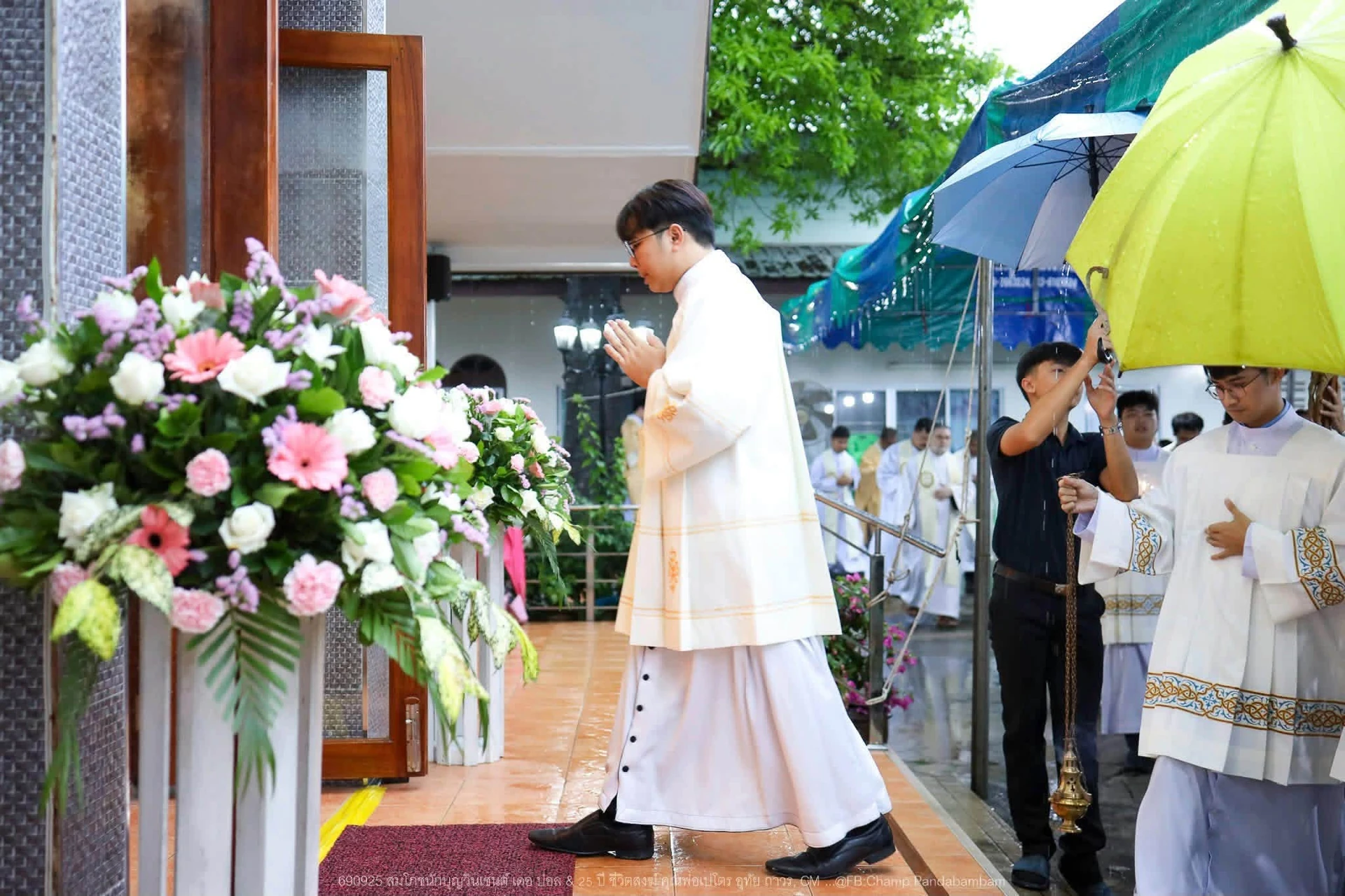 ผู้คนบริเวณทางเข้าที่ตกแต่งดอกไม้และมีร่ม จากรายงานสมโภชนักบุญวินเซนต์ เดอ ปอล สามพราน ปี 2569