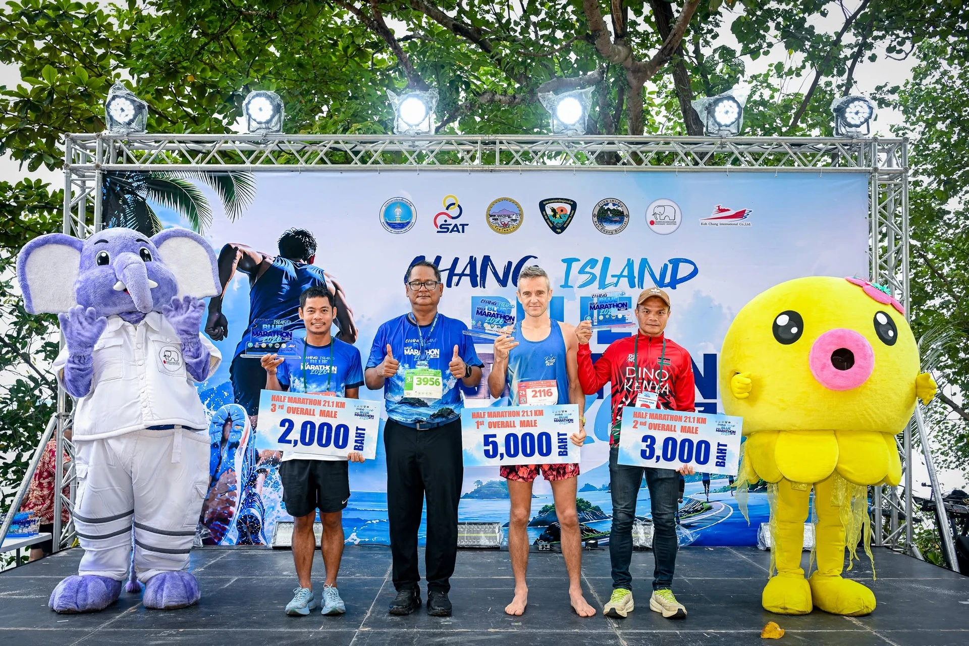กลุ่มบนเวทีถือป้ายรางวัลและมีมาสคอตสองข้าง ฉาก Chang Island Blue Half Marathon 2026