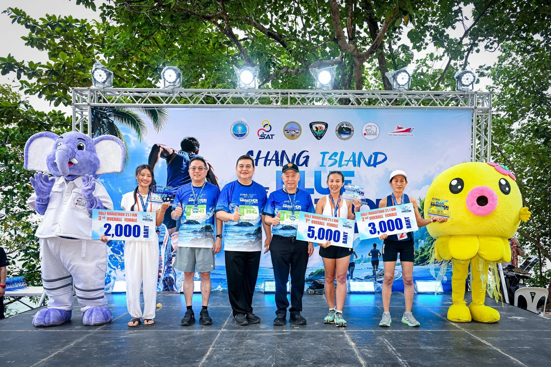 กลุ่มอีกภาพบนเวทีพร้อมป้ายรางวัลและมาสคอต ฉาก Chang Island Blue Half Marathon 2026
