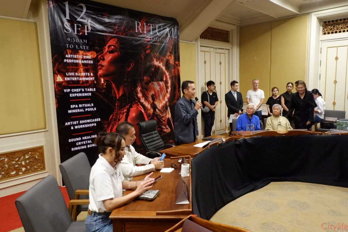 ภาพกว้างผู้ร่วมงานและผู้พูดถือไมโครโฟนในงานแถลงข่าว The Ritual 2026 ฉากยังระบุวันเดิม 12 กันยายน
