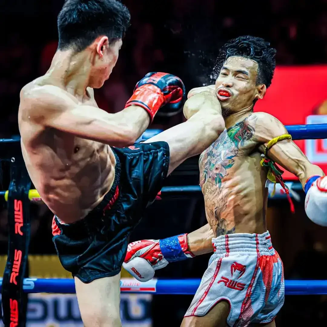 นักมวยแลกแข้งบนเวทีที่มีตรา RWS จากแกลเลอรีทางการ Rajadamnern World Series ไม่ระบุวันแข่งขัน
