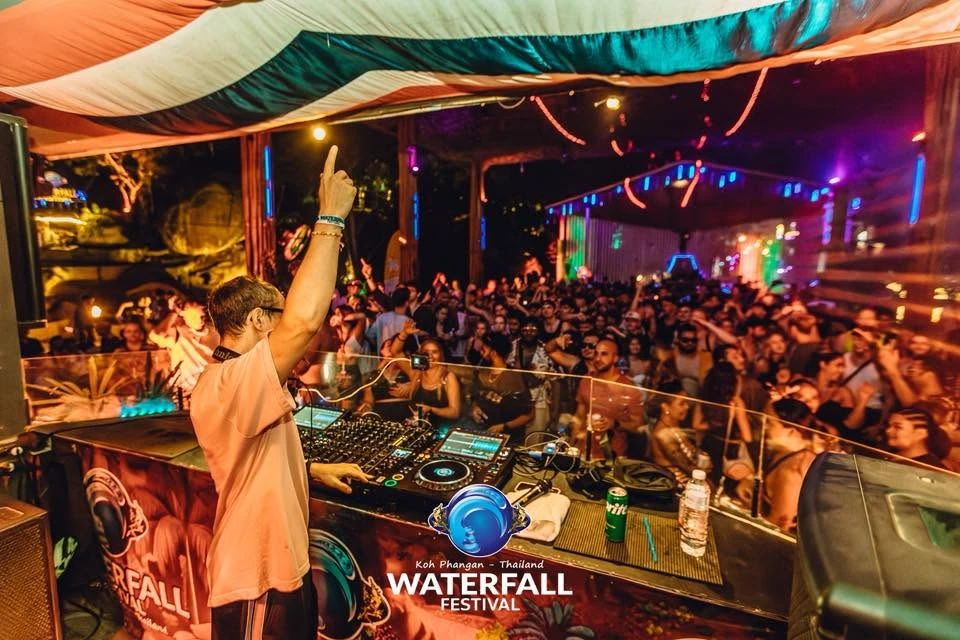 ดีเจเสื้อสีส้มยกแขนหน้าเครื่องเล่นและผู้ชม จากแกลเลอรีซีรีส์ Waterfall Festival ไม่ระบุวันถ่าย