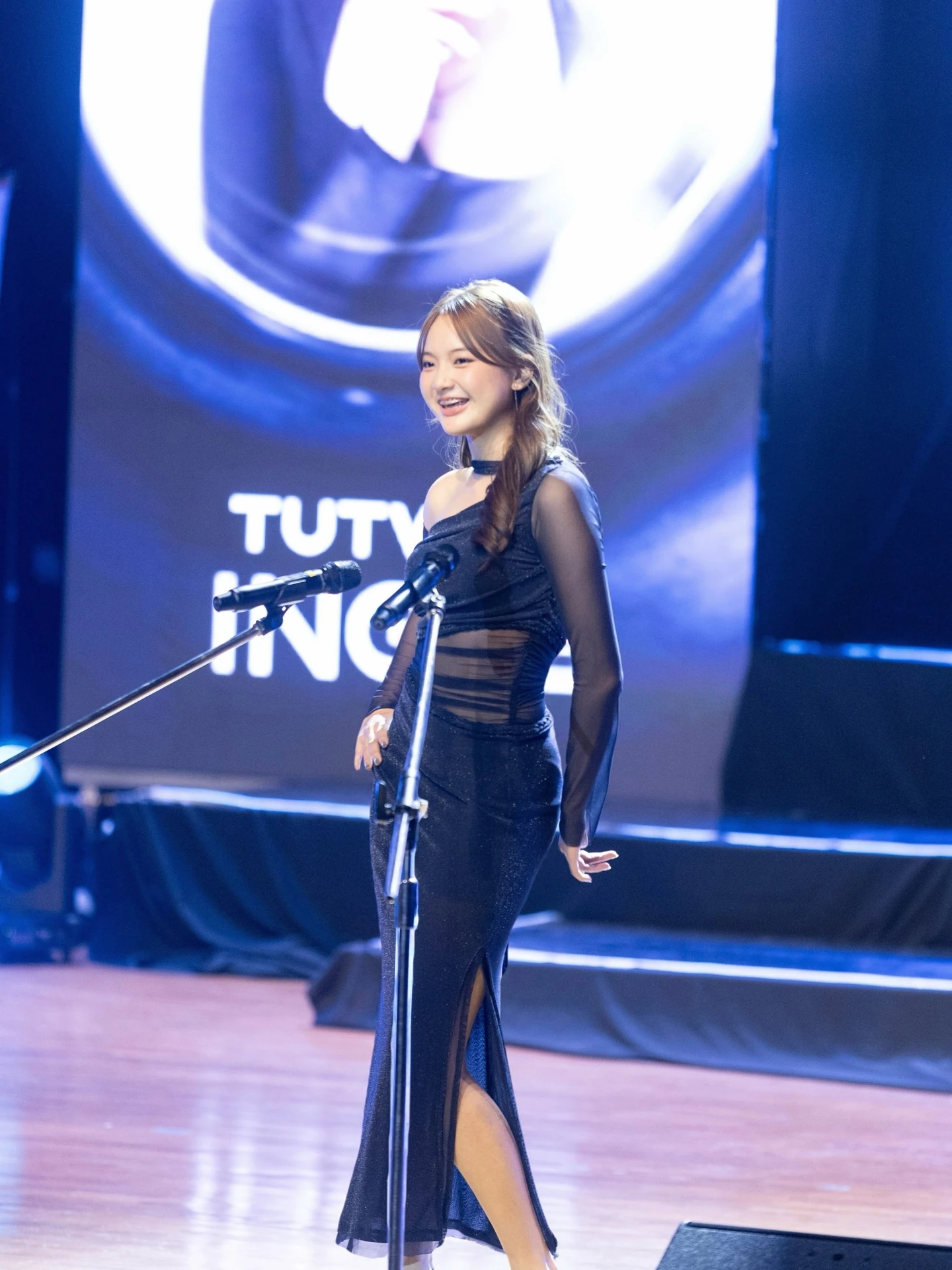 ผู้ร่วมกิจกรรมในชุดสีดำที่ไมโครโฟนบนเวที TUTV จากโพสต์รุ่นที่ 14 ไม่ระบุวันถ่าย