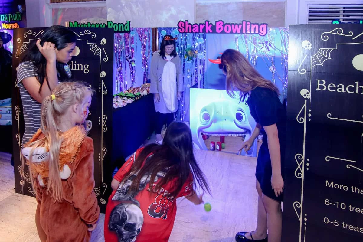 เด็กและผู้ใหญ่เล่นเกมโยนบอลหน้าบูธ Shark Bowling ในกิจกรรมฮาโลวีน Royal Cliff จากภาพที่ไม่ระบุวันถ่าย