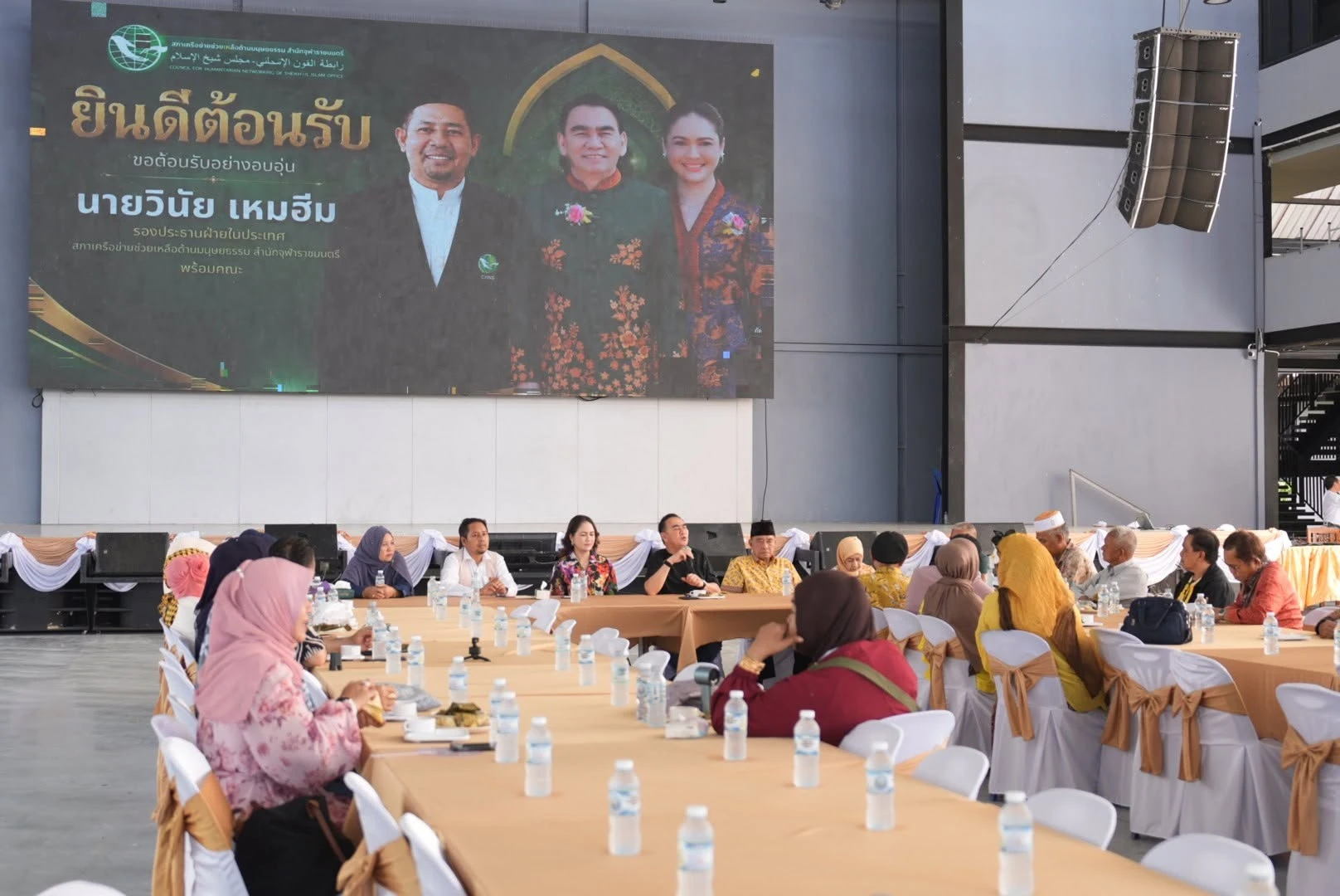 ผู้ร่วมการพบปะนั่งรอบโต๊ะใต้ป้ายต้อนรับสภาเครือข่ายช่วยเหลือด้านมนุษยธรรม ภาพเตรียมงานปัน พลังปันที่สงขลา