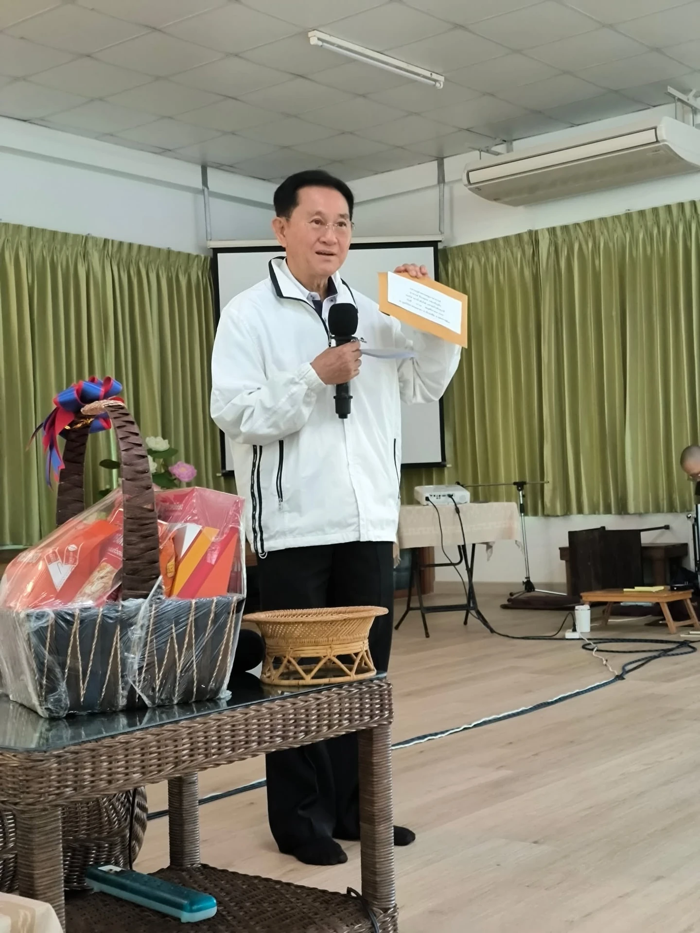 ผู้บรรยายถือไมโครโฟนและเอกสาร จากคอร์สเอาน้ำดับไฟ…เอาอะไรดับทุกข์ พฤศจิกายน 2568