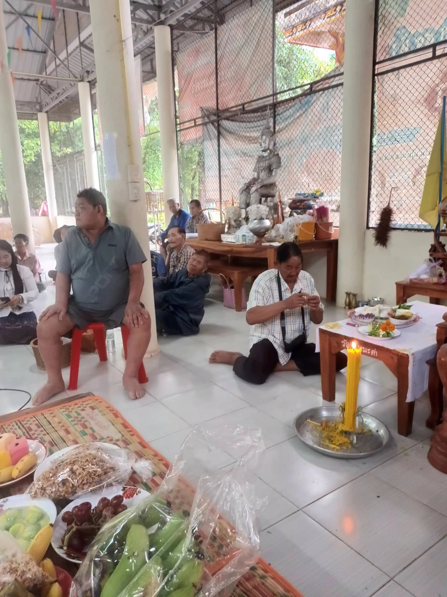 ผู้ร่วมทำบุญนั่งในศาลาใกล้เทียนและอาหาร จากโพสต์ระดมบุญค่ามีดตัดหวายลูกนิมิตวัดเนินมะค่า ปี 2569