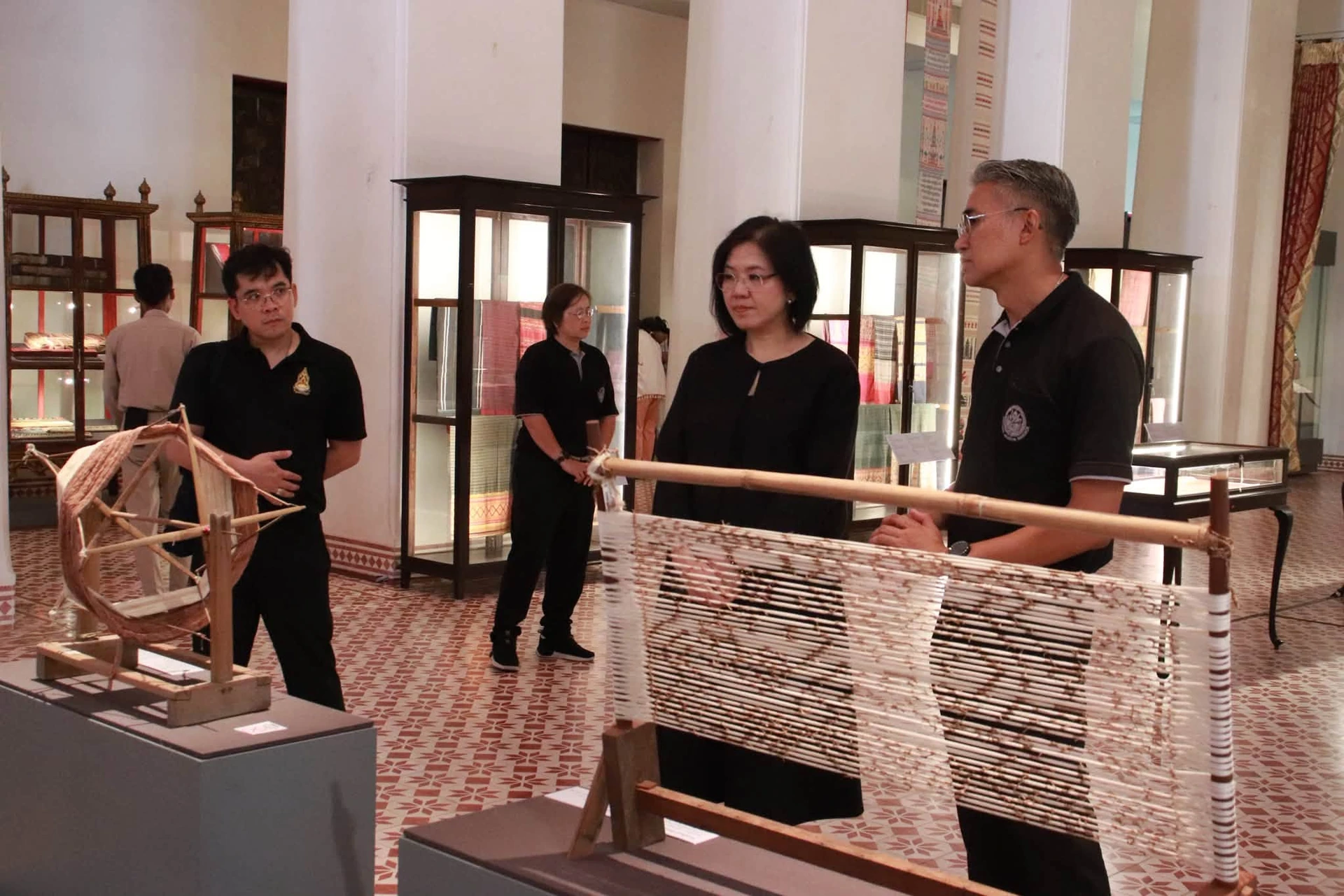 ผู้เข้าชมและผู้บรรยายบริเวณอุปกรณ์เกี่ยวกับการทอผ้าในนิทรรศการสยามพัสตราภรณ์พิไล จากรายงานวันที่ 17 กันยายน 2569