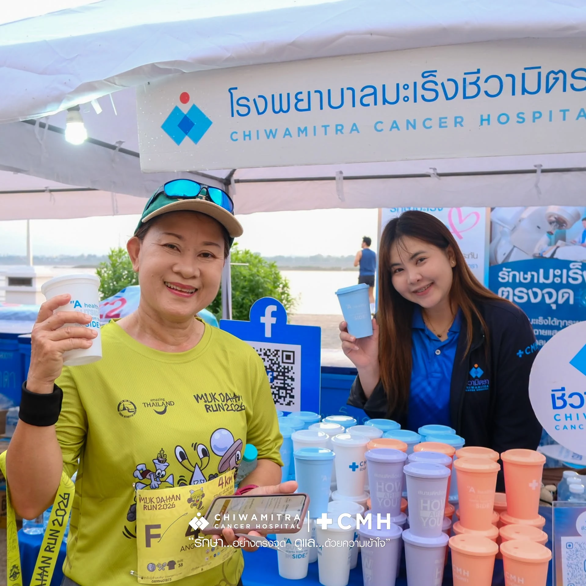 ผู้ร่วมงานถือแก้วข้างโต๊ะแก้วที่บูธชีวามิตรา จากรายงานการสนับสนุน Mukdahan Run วันที่ 27 กันยายน 2569